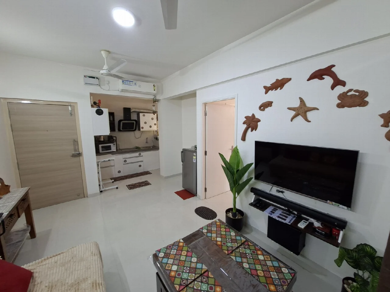 The Beginning’s living room with its patterned table, TV, terracotta wall decorations and adjoining kitchen
