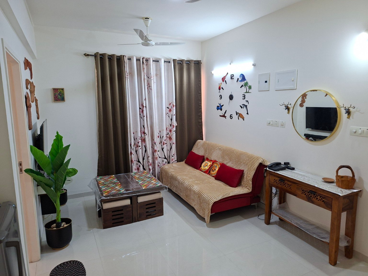 The Beginning living room with its sofa, patterned coffee table and colourful wall clock