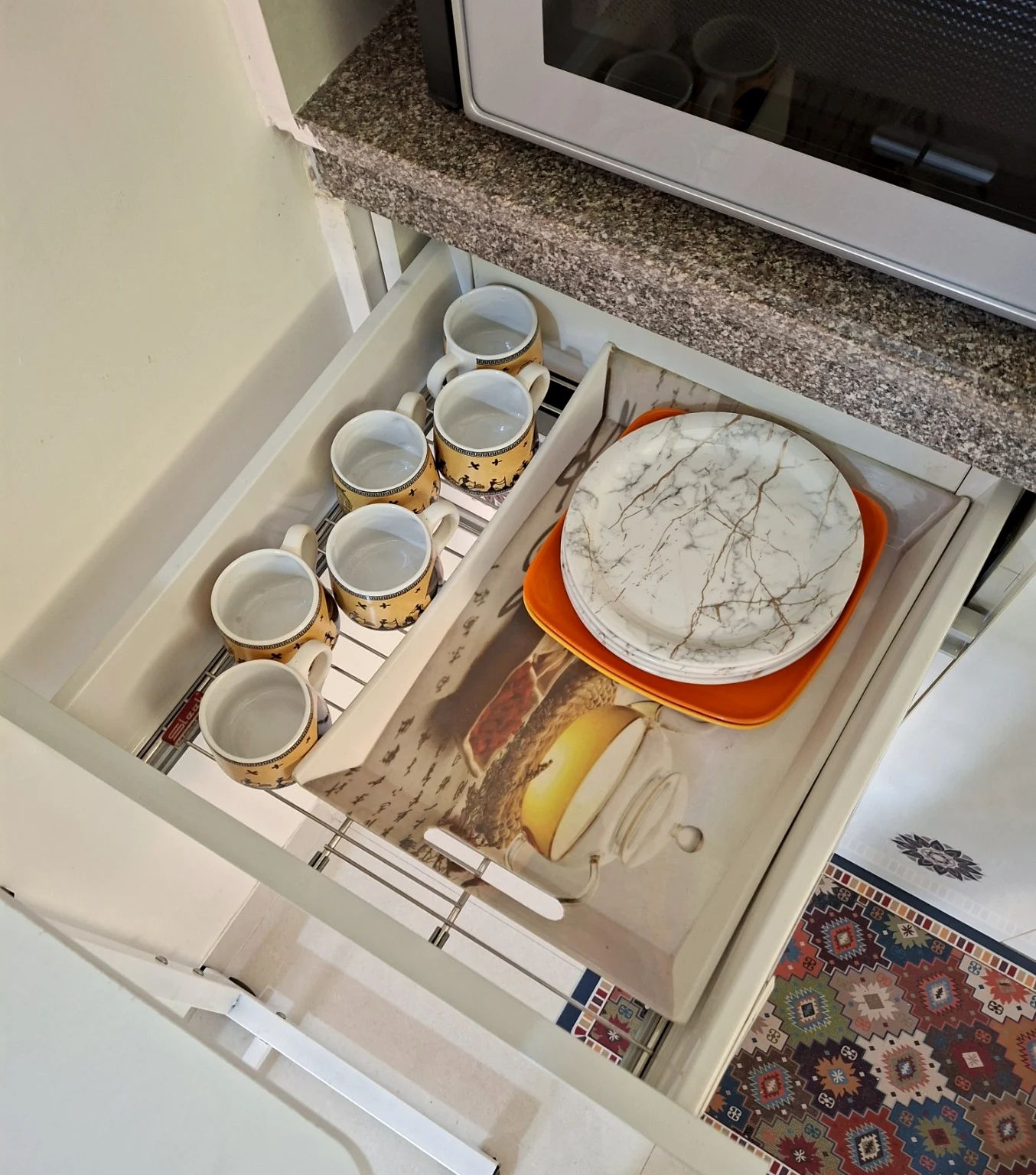 Open kitchen drawer containing mugs, plates and a serving tray