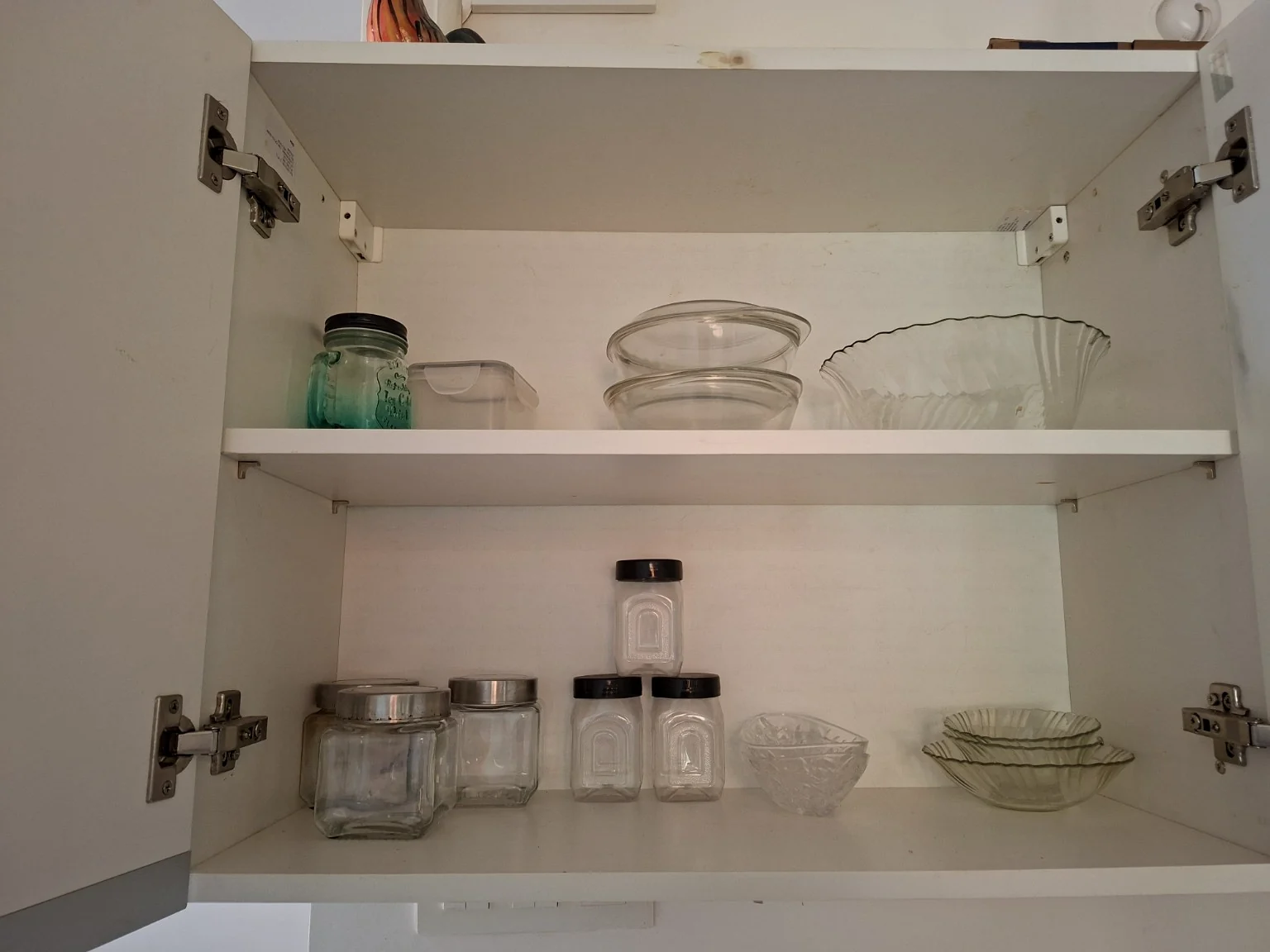 Open cupboard with glass bowls, jars and storage containers